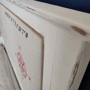 tête de lit en bois blanc capitonnée. La carte de l'île d'Yeu avec le nom des plages a été dessiné sur le tissu. On voit une rose des vents en rouge