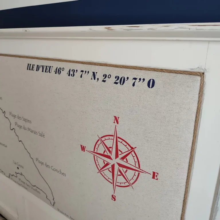 tête de lit en bois blanc capitonnée. La carte de l'île d'Yeu avec le nom des plages a été dessiné sur le tissu. On voit une rose des vents en rouge