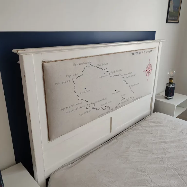 tête de lit en bois blanc capitonnée. La carte de l'île d'Yeu avec le nom des plages a été dessiné sur le tissu. On voit une rose des vents en rouge