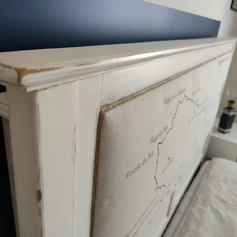 tête de lit en bois blanc capitonnée. La carte de l'île d'Yeu avec le nom des plages a été dessiné sur le tissu. On voit une rose des vents en rouge