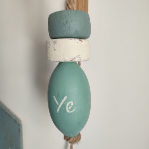 3 flotteurs de pêche de couleur vert céladon, gris vert et blanc suspendus à une corde en jute. On peut lire YE sur un flotteur.