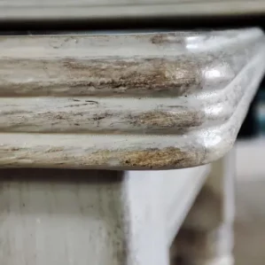 Détail du chan du plateau restauré d'une petite table gigogne. On voit bien la restauration avec la peinture de couleur beige et la patine avec de la cire bronze appliquée
