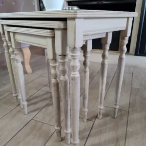 3 petites tables gigognes repliées. Elles sont de couleur beige patiné.