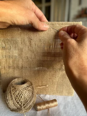 gros plan de main à coudre un tissu en jute. Au premier plan une bobine de corde de jute