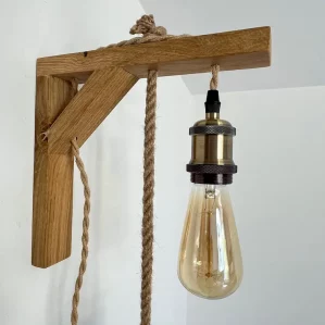 applique murale lumineuse accrochée sur mur blanc. Elle est composée d'une potence en bois clair, douille laiton, ampoule à filament.