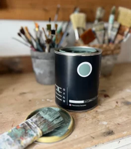 pot de peinture vert sauge devant pot avec pinceaux. Au premier plan un pinceau avec peinture sur les poils