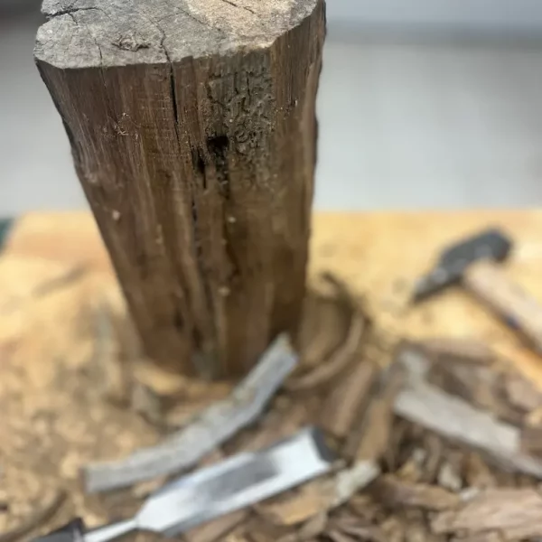 gros plan d'une poutre en bois en cours de rabotage. On voit des ciseaux à bois et des copeaux sur la table de l'atelier