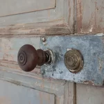 gros plan d'une poignée de porte ancienne en bois marron foncé. La porte est ancienne aussi. La patine de la peinture est magnifique, dans les tons de gris vert