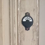 gros plan d'un verrou de porte ancienne en métal noir. On peut lire "libre" sur le verrou. La porte est ancienne aussi. Elle est de couleur kaki