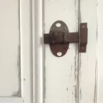gros plan d'un verrou de porte ancienne en métal rouillé. La porte est ancienne aussi. Elle est de couleur blanche