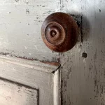 gros plan d'une poignée de porte ancienne en bois marron foncé. La porte est ancienne aussi. La patine de la peinture est magnifique, dans les tons de kaki