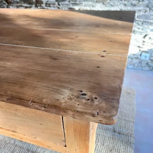 gros plan du plateau d'une table de ferme présentée devant un mur en pierres apparentes. Belle patine de la table