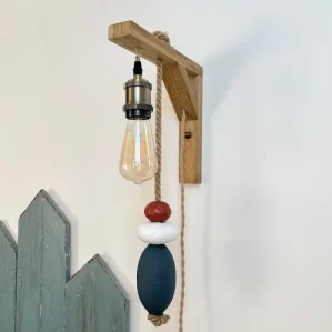 applique murale lumineuse. Composé d'une potence en bois clair. D'une douille de couleur laiton, d'une ampoule allongée à filament. De 3 flotteurs de pêche suspendus à une corde en jute