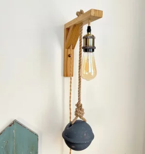 applique murale lumineuse accrochée sur mur blanc. Elle est composée d'une potence en bois clair, douille laiton, ampoule à filament, flotteur de pêche peint en gris bleuté. A côté on voit des planches en bois peintes en vert céladon et fixées au mur
