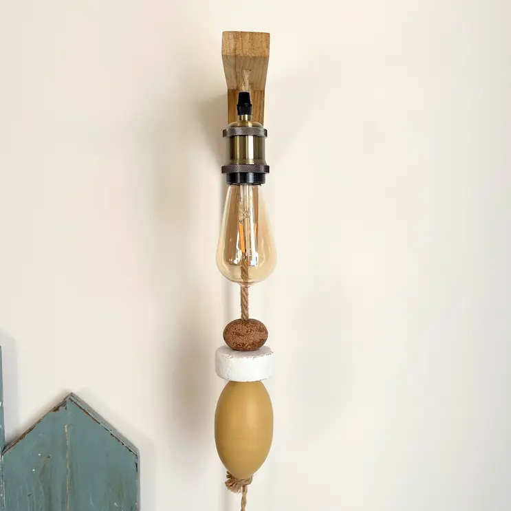 applique murale lumineuse. Composé d'une potence en bois clair. D'une douille de couleur laiton, d'une ampoule allongée à filament. De 3 flotteurs de pêche suspendus à une corde en jute