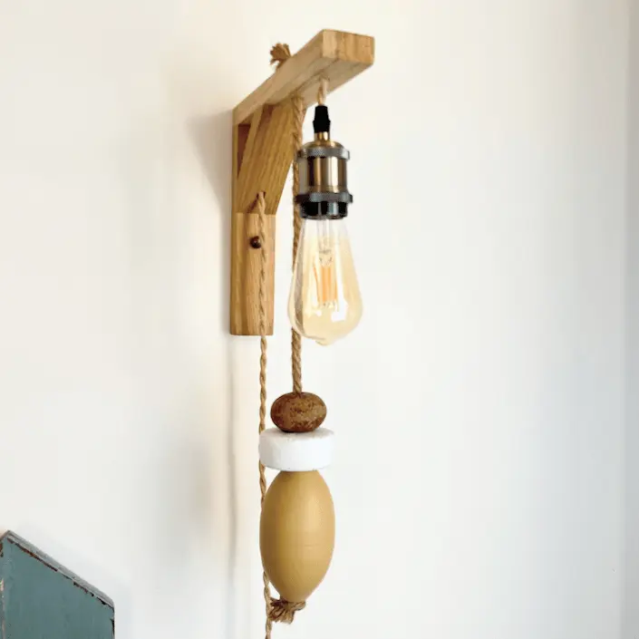 applique murale lumineuse. Composé d'une potence en bois clair. D'une douille de couleur laiton, d'une ampoule allongée à filament. De 3 flotteurs de pêche suspendus à une corde en jute